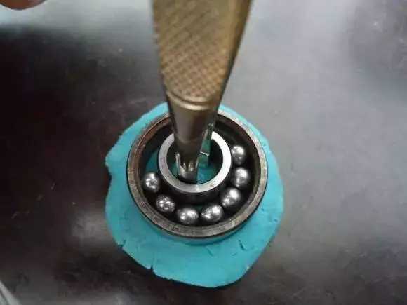 用鑷子或別的相近的物體越過內圈，同時向滾珠的方向用力頂住